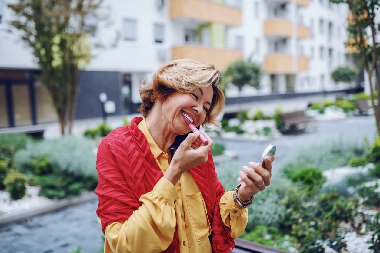 woman smiling putting lipstick on outside